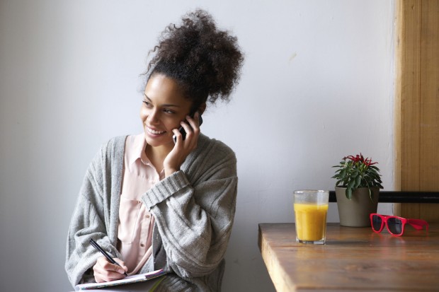 Portrait of a young african american woman talking on mobile phone and taking notes