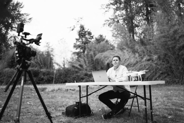 Man sitting at a table outdoors with his computer, drone, and video camera