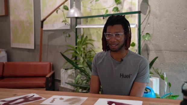 Raven Guenneguez sits as a desk with his art talking about creative stress.