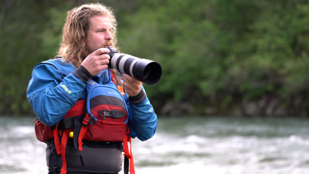 Riley Seebeck holds a camera at the side of a river